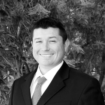 a man in a suit and tie standing in front of a tree