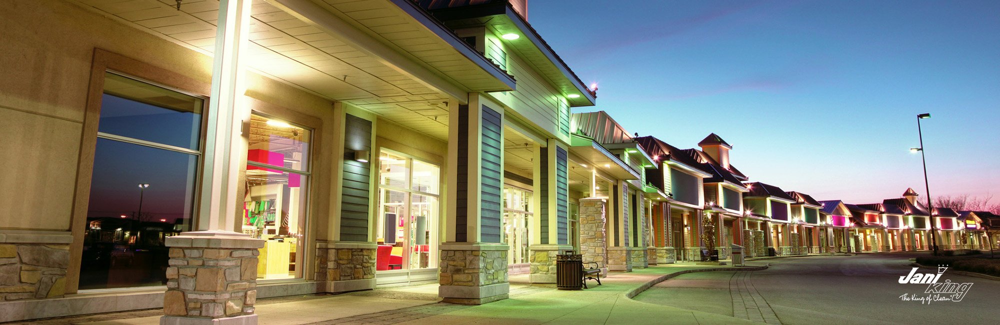 Line of local businesses illuminated with their store lighting as night time is starting.